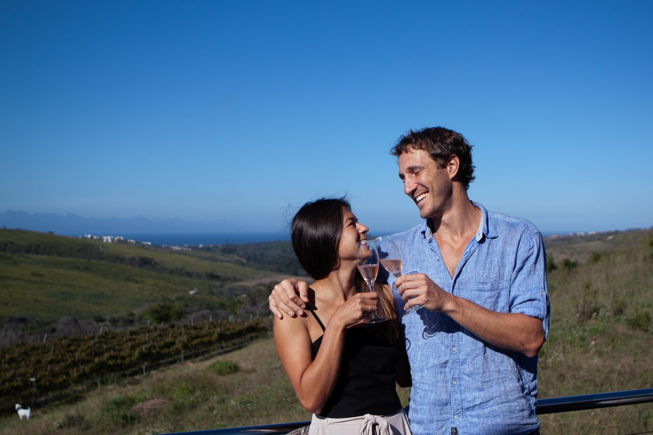 Engagement ring blog post cover image of Kim and Chris cheersing at a wine farm in Plettenberg Bay